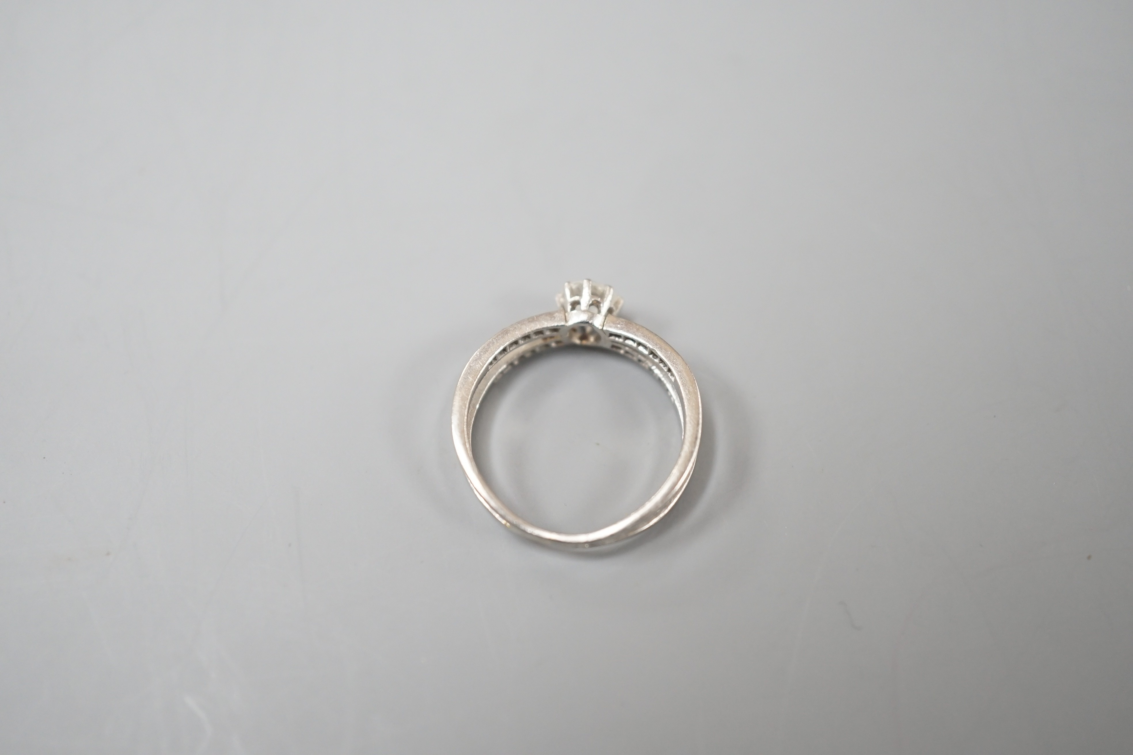 A modern white metal and single stone diamond ring, with diamond chip set crossover shoulders, size K, gross weight 3.3 grams.